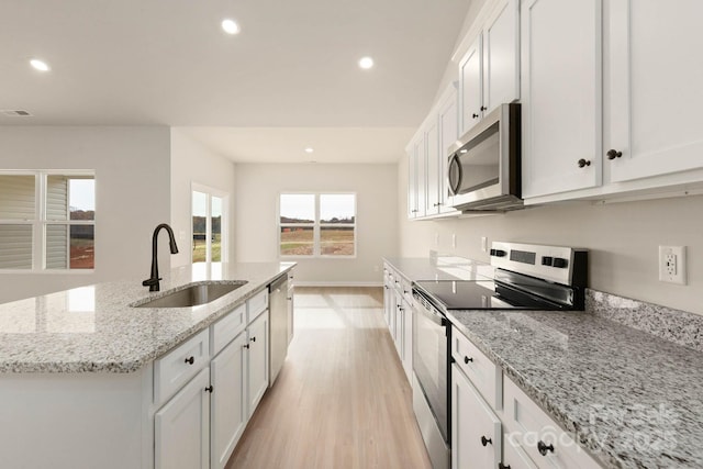 kitchen with a kitchen island with sink, white cabinets, sink, light stone countertops, and appliances with stainless steel finishes