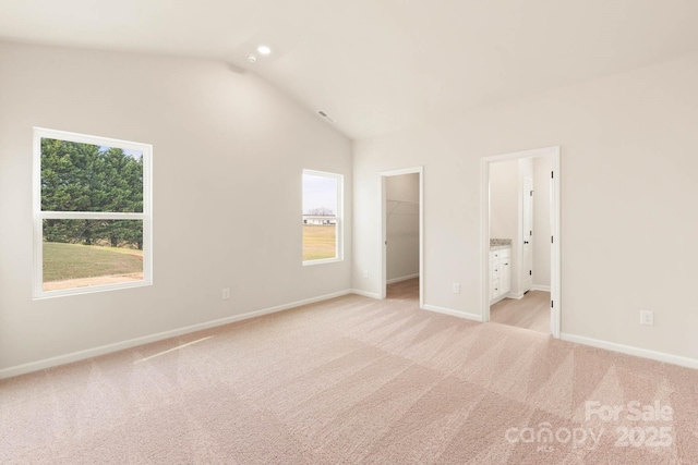 unfurnished bedroom featuring connected bathroom, a spacious closet, lofted ceiling, light carpet, and a closet