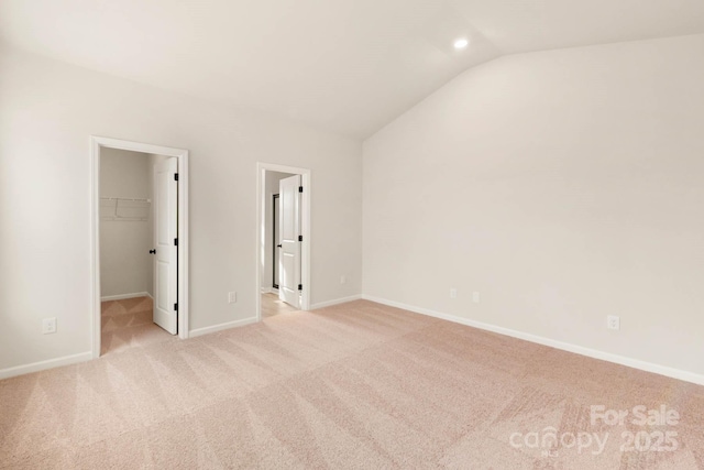 unfurnished bedroom featuring a walk in closet, a closet, light colored carpet, and lofted ceiling