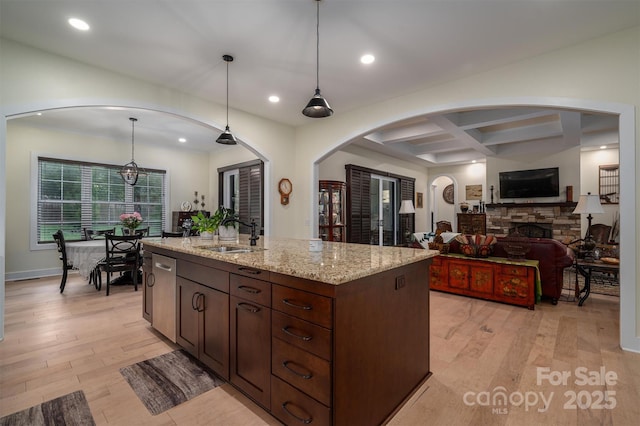 kitchen with coffered ceiling, a stone fireplace, sink, beamed ceiling, and decorative light fixtures