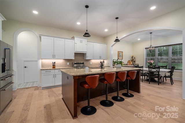 kitchen featuring a kitchen island with sink, white cabinets, hanging light fixtures, and appliances with stainless steel finishes