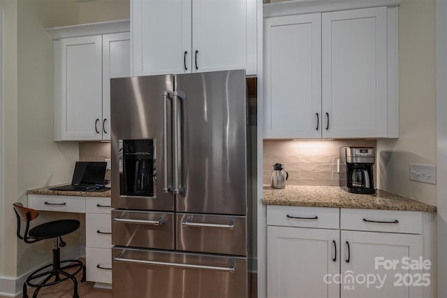 kitchen featuring backsplash, stainless steel fridge, white cabinets, and light stone countertops