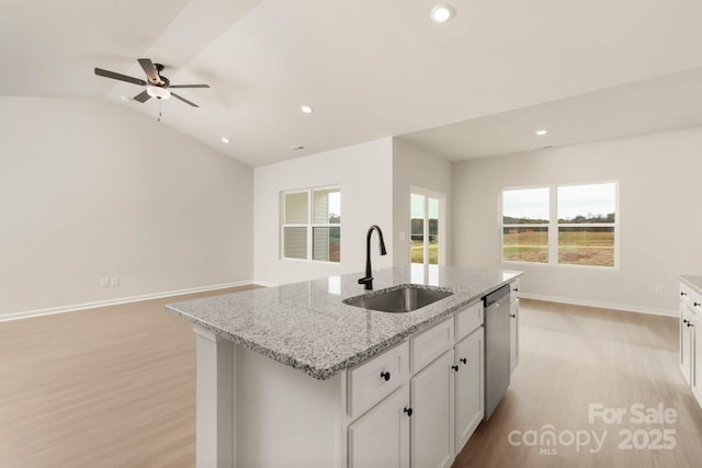 kitchen featuring dishwasher, lofted ceiling, a center island with sink, sink, and light stone countertops