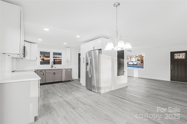 kitchen with appliances with stainless steel finishes, sink, white cabinets, light hardwood / wood-style floors, and hanging light fixtures