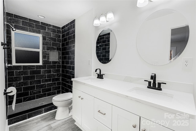 bathroom with hardwood / wood-style floors, vanity, a tile shower, and toilet