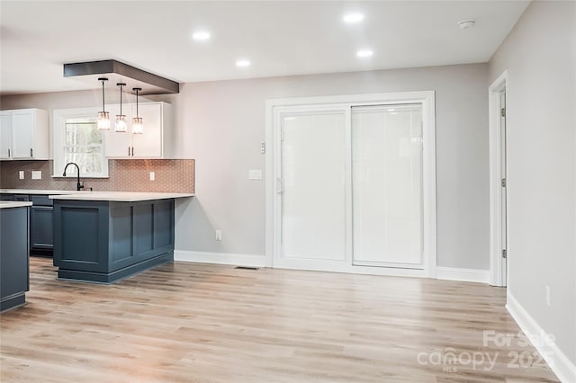 kitchen featuring white cabinetry, decorative light fixtures, light wood-type flooring, and tasteful backsplash