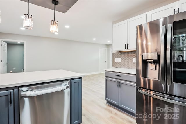 kitchen with appliances with stainless steel finishes, light wood-type flooring, pendant lighting, white cabinets, and tasteful backsplash