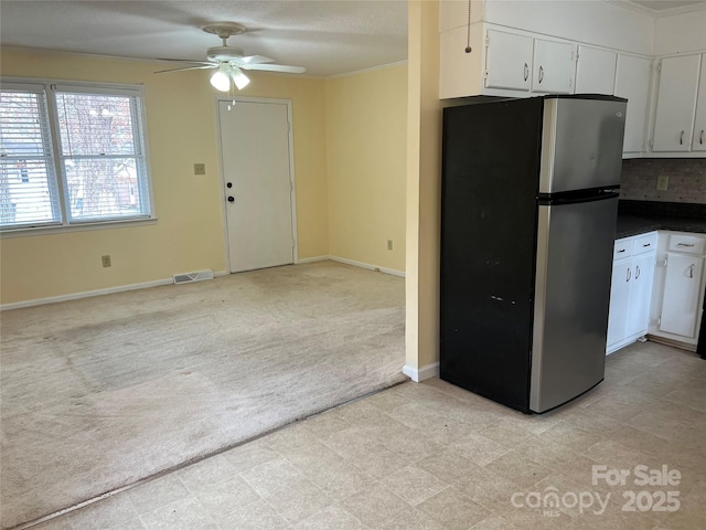 kitchen featuring dark countertops, visible vents, light carpet, freestanding refrigerator, and white cabinetry