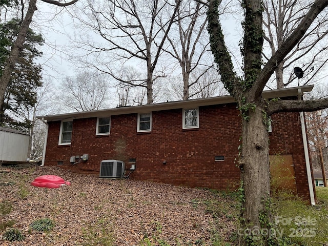 rear view of property with central air condition unit, brick siding, and crawl space