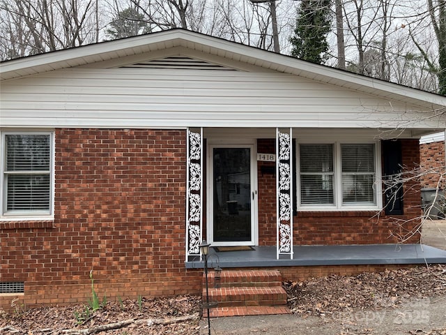 entrance to property featuring covered porch, brick siding, and crawl space