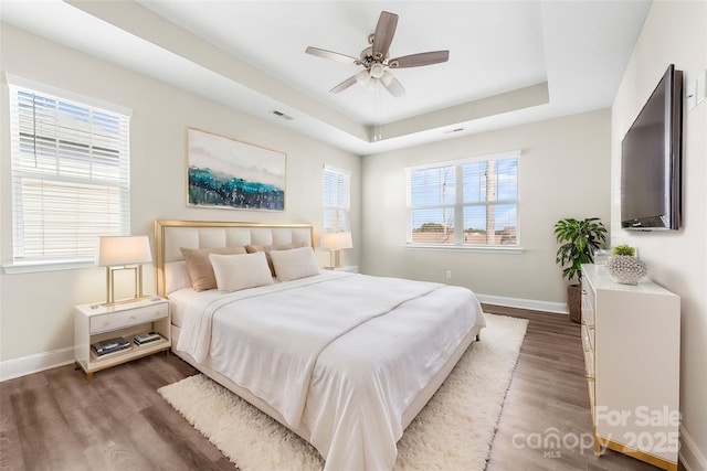 bedroom with ceiling fan, dark hardwood / wood-style floors, and a raised ceiling