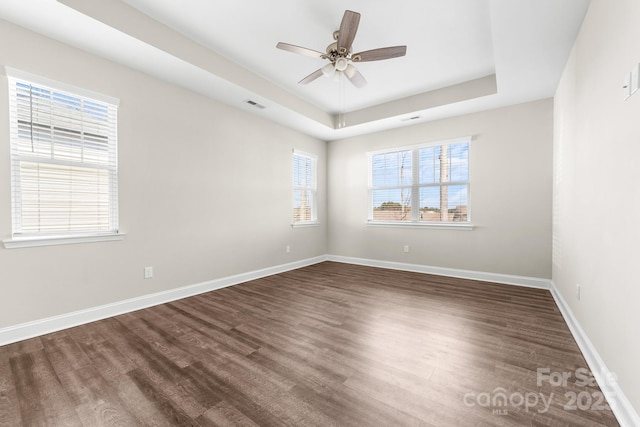 unfurnished room featuring dark wood-type flooring, a healthy amount of sunlight, a raised ceiling, and ceiling fan