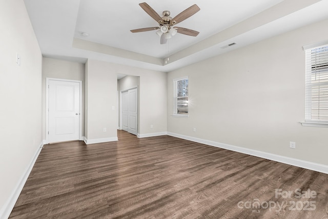 unfurnished bedroom with a raised ceiling, ceiling fan, dark hardwood / wood-style flooring, and multiple windows