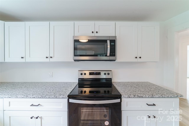 kitchen with light stone countertops, light hardwood / wood-style flooring, white cabinets, and stainless steel appliances