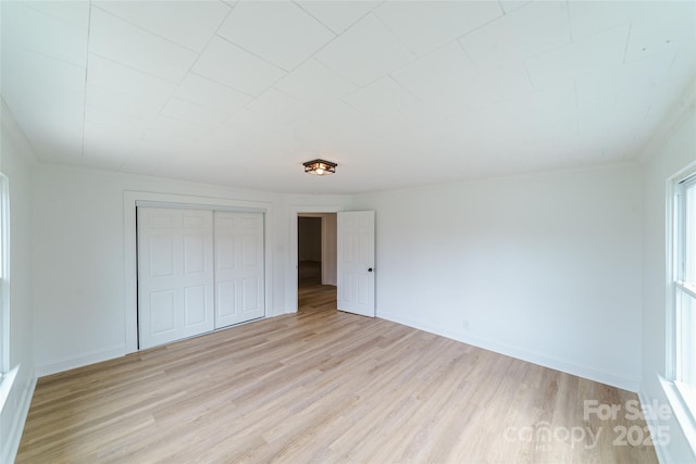 unfurnished bedroom featuring crown molding, a closet, and light wood-type flooring