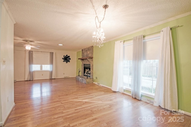 unfurnished living room with ceiling fan with notable chandelier, a stone fireplace, crown molding, and light hardwood / wood-style flooring