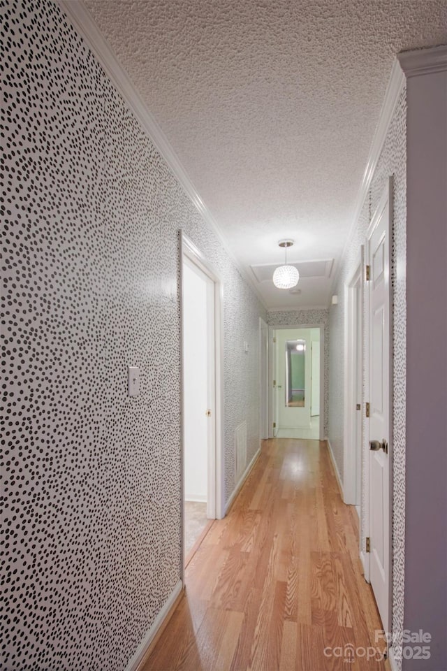 corridor with light hardwood / wood-style floors, a textured ceiling, and ornamental molding