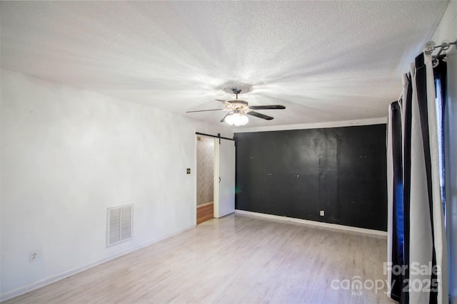 spare room featuring ceiling fan, a barn door, light wood-type flooring, and a textured ceiling