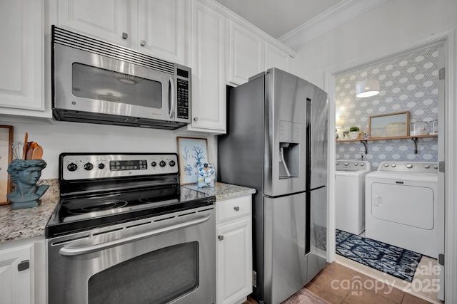 kitchen with washing machine and clothes dryer, white cabinetry, stainless steel appliances, dark tile patterned floors, and ornamental molding