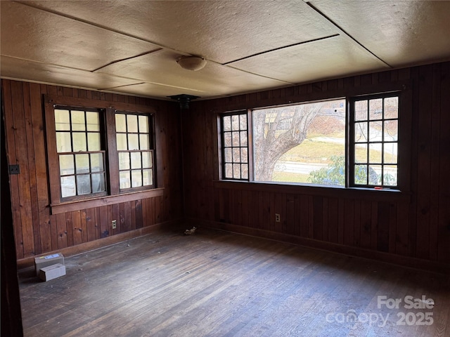 empty room featuring wooden walls, dark hardwood / wood-style flooring, and a textured ceiling