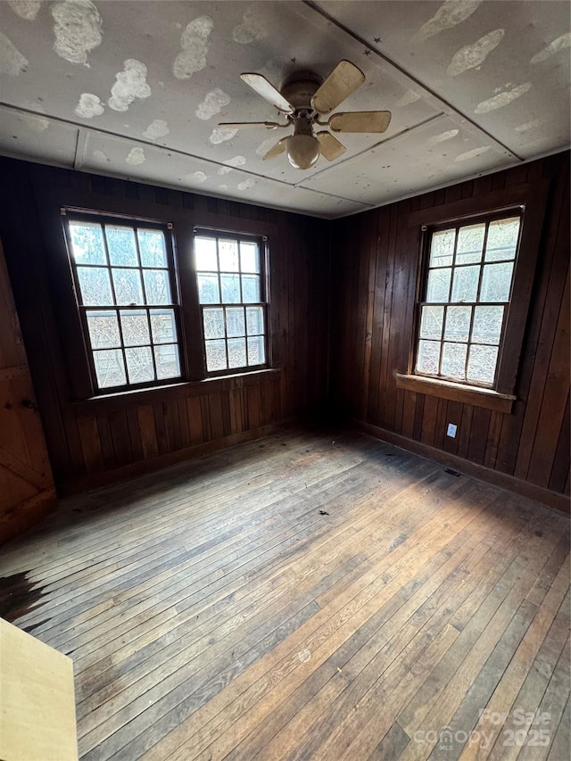 unfurnished room featuring wooden walls, light hardwood / wood-style floors, and ceiling fan