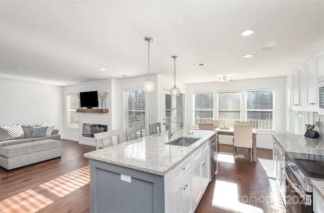 kitchen featuring light stone countertops, sink, white cabinetry, and a center island with sink