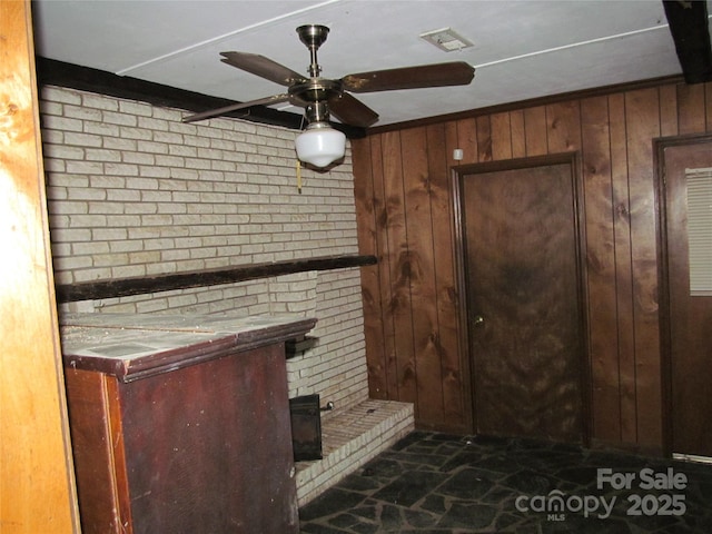 unfurnished living room with ceiling fan, wooden walls, and brick wall