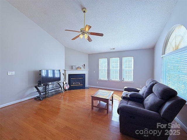 living room featuring vaulted ceiling, ceiling fan, wood-type flooring, and a textured ceiling