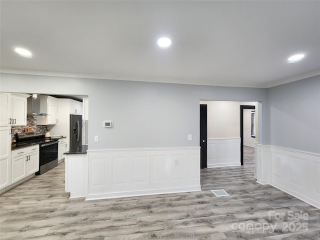 kitchen with white cabinetry, stainless steel electric stove, fridge with ice dispenser, ornamental molding, and wall chimney exhaust hood