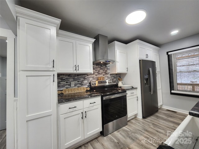 kitchen featuring light hardwood / wood-style floors, stainless steel appliances, backsplash, wall chimney range hood, and white cabinets