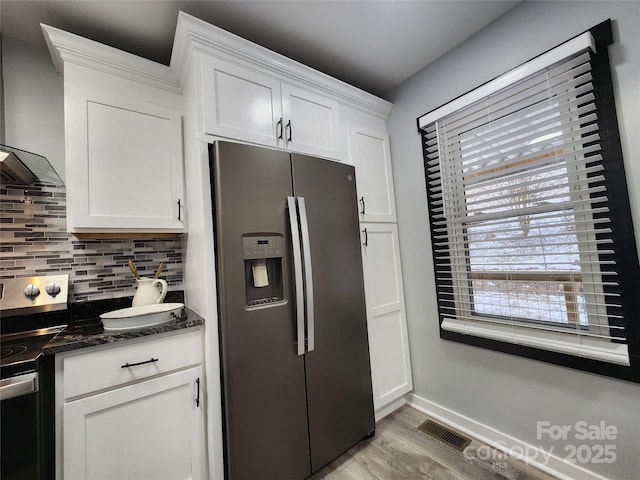 kitchen featuring tasteful backsplash, wall chimney range hood, white cabinetry, light wood-type flooring, and appliances with stainless steel finishes