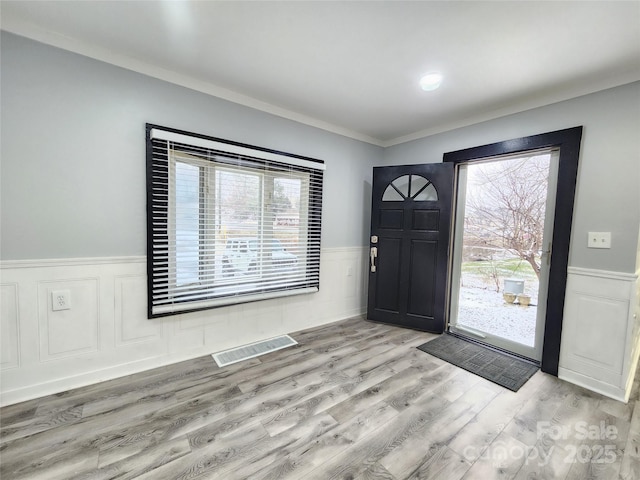 entrance foyer featuring a wealth of natural light, ornamental molding, and light hardwood / wood-style floors