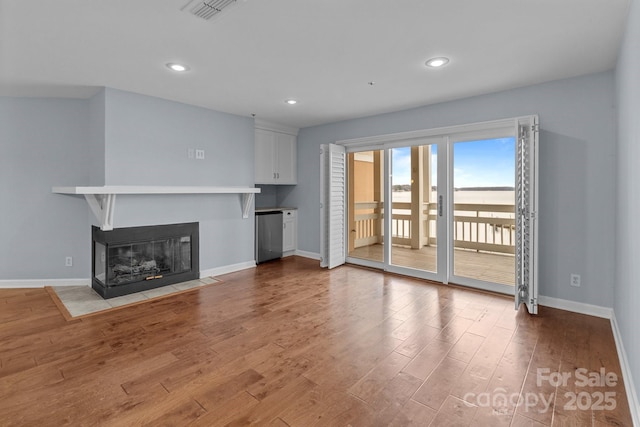 unfurnished living room featuring a multi sided fireplace, baseboards, wood finished floors, and visible vents