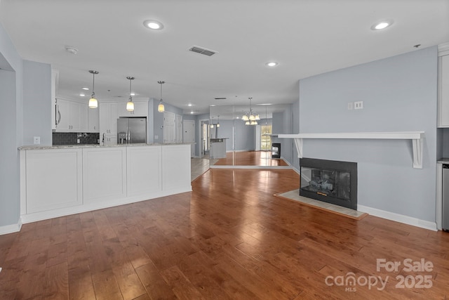 unfurnished living room with a chandelier, baseboards, visible vents, and a multi sided fireplace