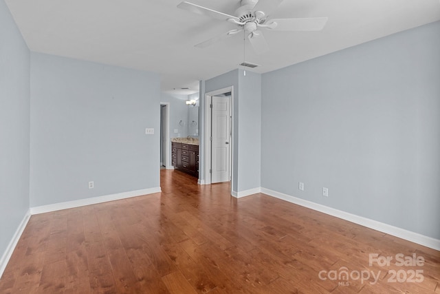 empty room with wood finished floors, visible vents, a ceiling fan, and baseboards