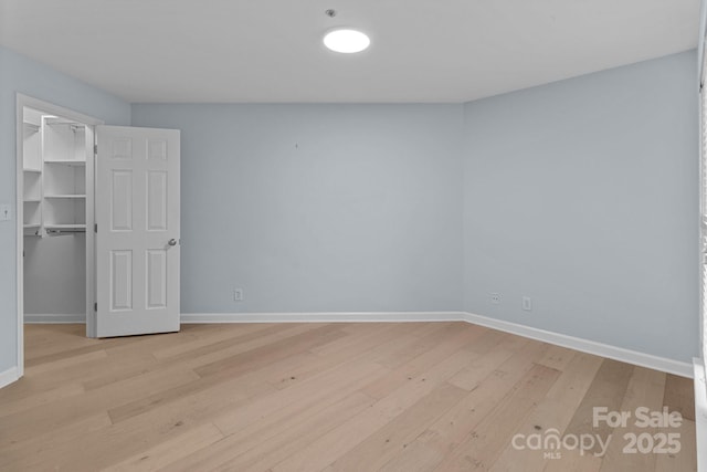 unfurnished bedroom with baseboards, a spacious closet, light wood-style floors, and a closet