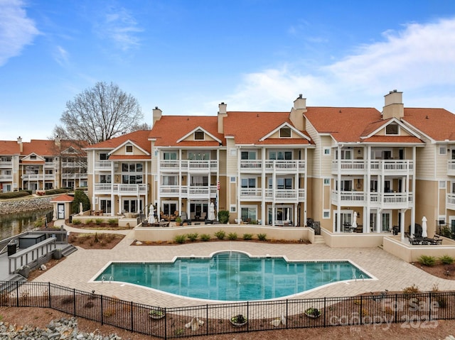 rear view of property featuring a community pool, fence, and a patio