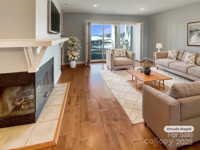 living area featuring a fireplace with flush hearth, baseboards, wood finished floors, and recessed lighting