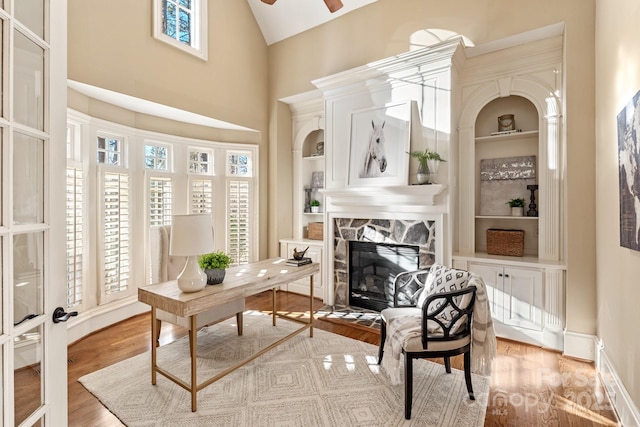 office area featuring built in shelves, light wood-type flooring, and a stone fireplace