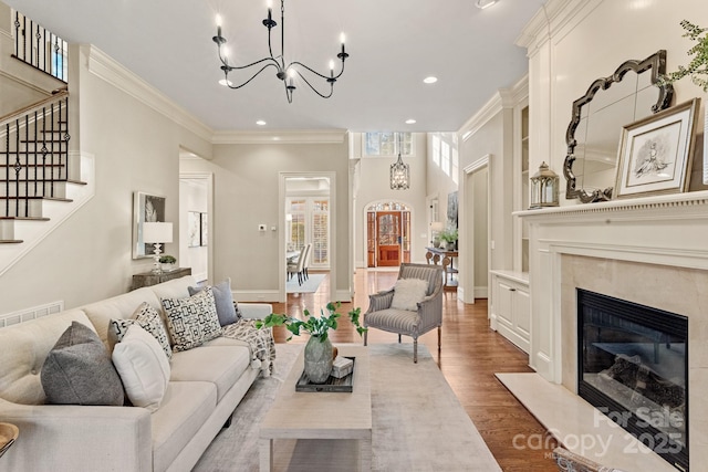 living room featuring wood-type flooring, a chandelier, a premium fireplace, and ornamental molding