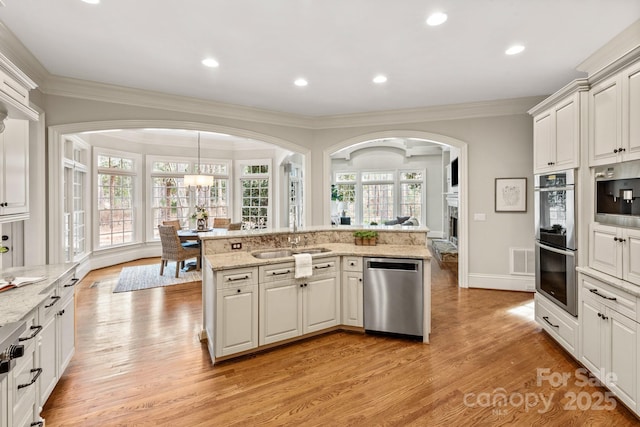 kitchen featuring sink, light wood-type flooring, decorative light fixtures, stainless steel appliances, and light stone counters