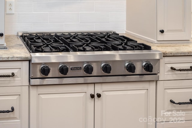 interior details featuring cooktop, white cabinetry, light stone countertops, and tasteful backsplash