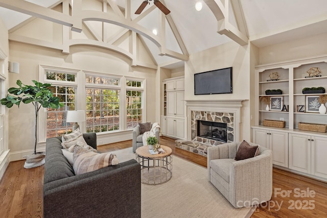 living room featuring high vaulted ceiling, ceiling fan, a stone fireplace, and light wood-type flooring