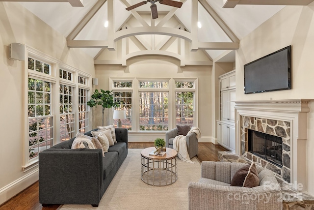 living room with ceiling fan, hardwood / wood-style floors, beamed ceiling, and a stone fireplace