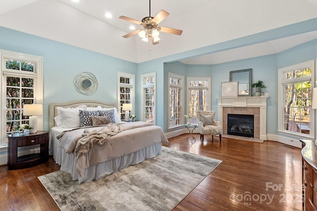 bedroom with ceiling fan, dark hardwood / wood-style flooring, high vaulted ceiling, and a tiled fireplace