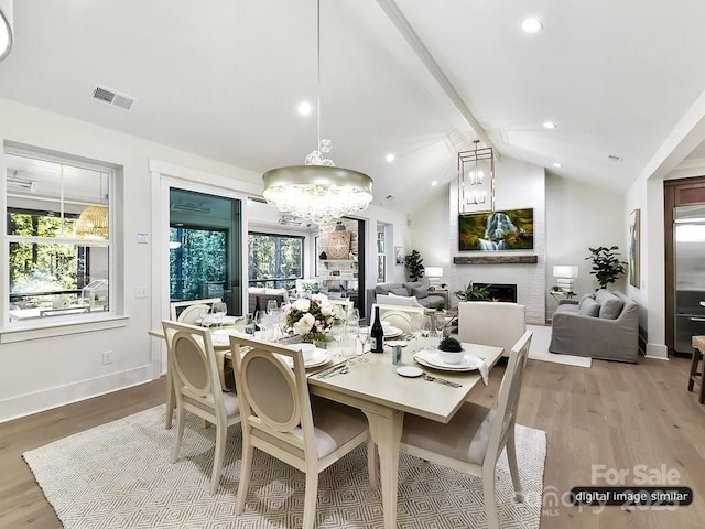 dining area featuring a fireplace, light hardwood / wood-style flooring, vaulted ceiling, and an inviting chandelier