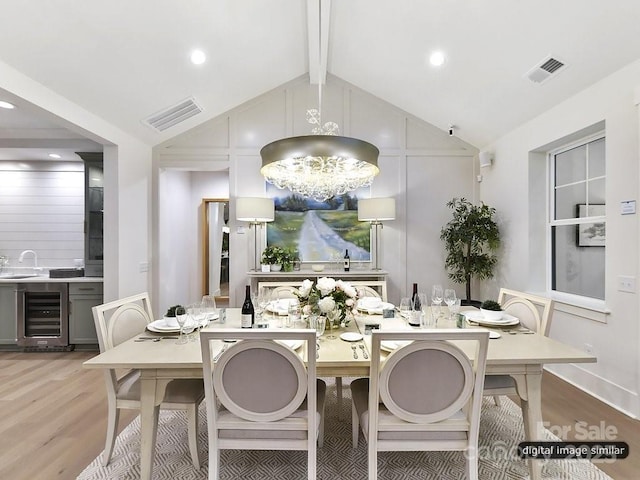 dining area with sink, vaulted ceiling with beams, a notable chandelier, light hardwood / wood-style floors, and beverage cooler