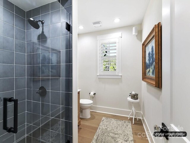 full bath with tiled shower, wood finished floors, baseboards, toilet, and recessed lighting