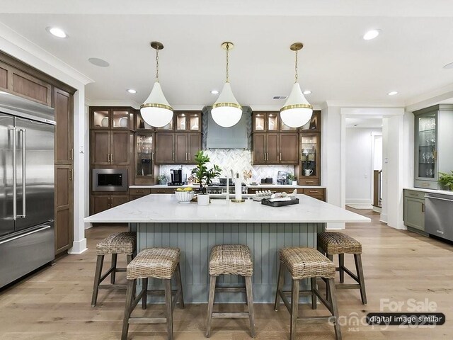 kitchen featuring built in appliances, decorative backsplash, custom range hood, a kitchen bar, and light wood-style floors