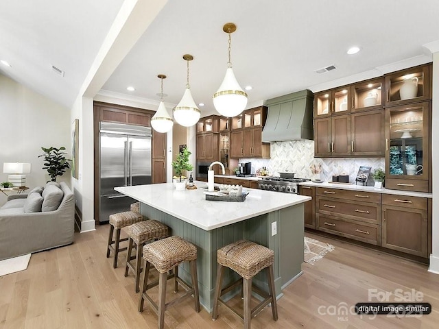 kitchen featuring custom exhaust hood, stainless steel built in refrigerator, a sink, a breakfast bar, and backsplash